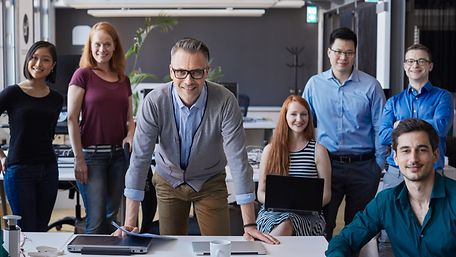 Mitarbeiter im Büro die stehende, wie auch sitzend lächeln und dynamisch auf die nächsten Aufgaben warten
